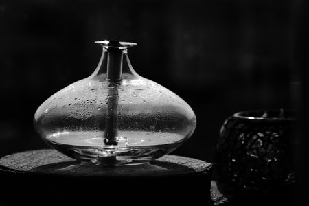 A minimalist black and white photograph featuring a sleek glass decorative kerosene lamp resting on a wooden surface.の写真素材