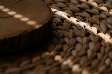 Natural wooden slice placed on textured woven straw mat with warm sunlight shadows, rustic eco-friendly organic background for interior design, handmade crafts, natural lifestyle.の写真素材