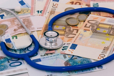 Stethoscope on a pile of bank notes and coins, analyzing health care costsの写真素材