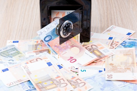 Black metal coin bank with bank notes on a deskの写真素材