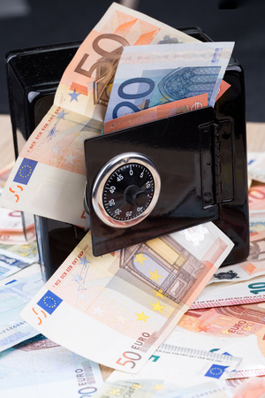Black metal coin bank with bank notes on a deskの写真素材
