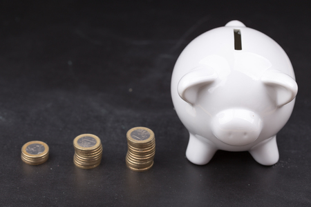 White piggy bank on a dark background, namely a blackboard with stacks of coins in increasing orderの写真素材
