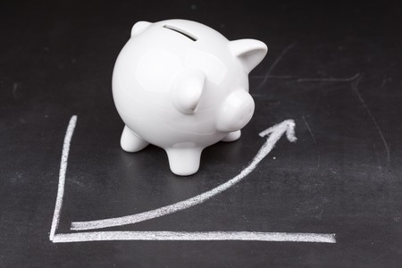 White piggy bank on a dark background, namely a blackboard with a graph showing growthの写真素材