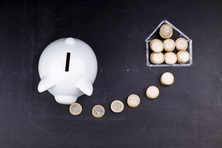 White piggy bank on blackboard: saving for a house, coins and a drawing of a houseの写真素材