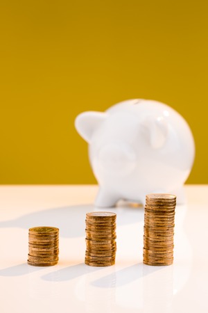 White piggy bank with a stack of coins and a yellow background