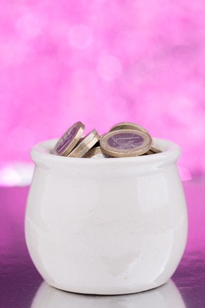 White ceramic pot full of coins on pink blurry backgroundの写真素材