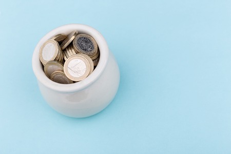 White pot full of coins on blue background from an high angleの写真素材
