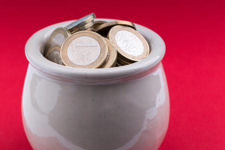 White pot full of coins on red background from an high angleの写真素材