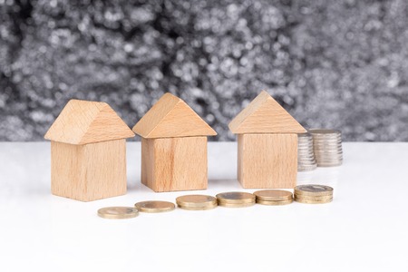 Three houses made of wooden blocks with a blurry background and coinsの写真素材