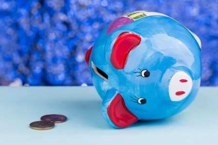 Blue piggy bank on a blue background: it's on its side with a few penny's, a concept of a tight budgetの写真素材