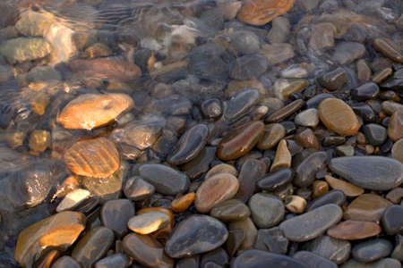 A pure transparent sea wave rolls over the rocky pebble shore, the concept of rest and travel,...