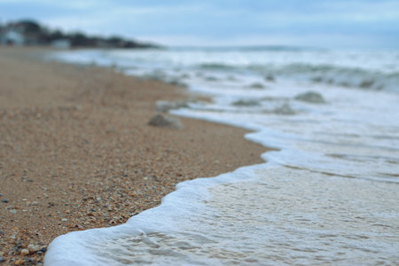 Sea wave rolls along the shore of a sandy beach, autumn footage of the seascape, blurred background, selective focus Sea of Azov, Russiaの写真素材