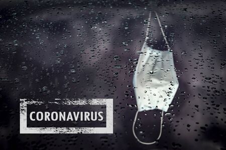 It's a nasty day. Drops of water on a car windshield. Medical mask behind the glass, sadness negative.の写真素材