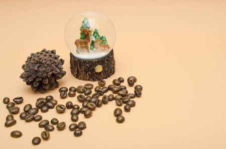 pine cone, glass bowl with three Christmas trees and two deers, sprinkled roasted gilded coffee beans on pastellgelb background copy spaceの写真素材