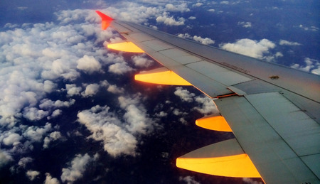 Wing of the plane, illuminated by the morning sun, against the background of clouds