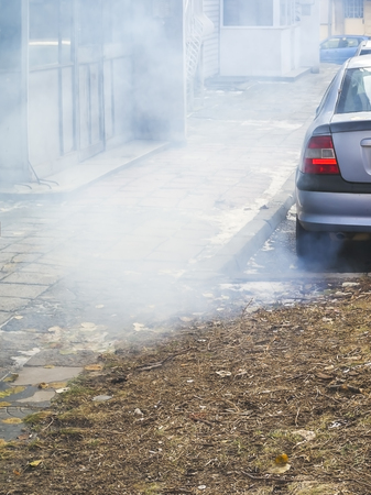 Large cloud of gray smoke from the exhaust pipe of a car in the courtyard of a residential building, ecology, urban smog, air pollution concept, horizontal vertical frame.の写真素材