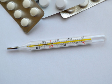Blisters with pills and a mercury thermometer with 37.4 degrees on a neutral background, close up,...
