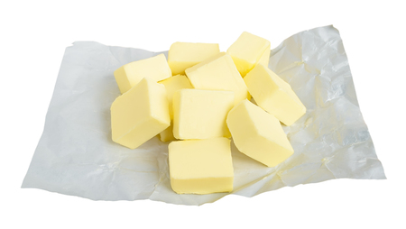 Fresh butter cut into pieces for making sauce or shortbread dough. Pieces of butter on white paper packaging. Natural fat nutrient. Isolated on white background. Front view.の写真素材