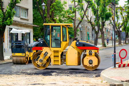 Yellow roller for tamping asphalt at the site of road construction works on a city street on a...