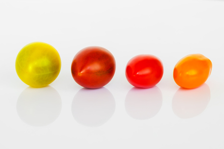 Close-up of yellow, brown, red and orange cherry tomatoes on a white glossy background. Mix of multicolored small and tasty tomatoes. Vegetables, vegetarian and healthy eating.の写真素材