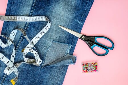 Blue jeans with large hole on a pant leg below the knee, multi coloured headed sewing pins, white...