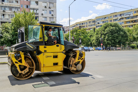 Varna, Bulgaria, June 22, 2019. Yellow roller for asphalt tamping moves on the city street to the new constraction site.  Road-building machinery. Improvement of urban roads.のeditorial素材