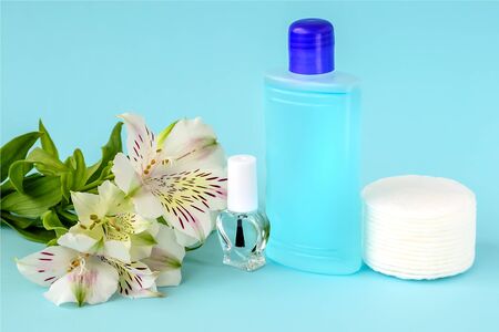 Glass bottle with colorless nail polish, plastic bottle with nail varnish remover, cotton pads and white flowers on a blue background. Manicure, pedicure, nail care products. Front view.の写真素材