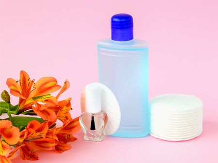 Glass bottle with colorless nail polish, plastic bottle with nail varnish remover, cotton pads and orange flowers on a pastel pink background. Manicure, pedicure, nail care products. Front view.の写真素材