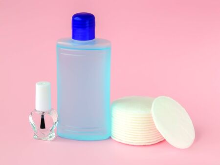 Glass bottle with colorless nail polish, plastic bottle with nail varnish remover and cotton pads on a pastel pink background. Manicure, pedicure, nail care products. Front view.の素材 [FY310127574679]