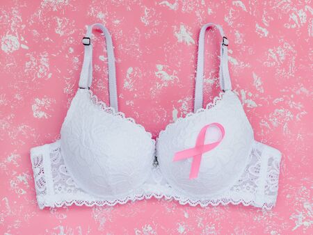 White lace bra with breast cancer awareness ribbon on a pastel pink background with white spots. Pink ribbon of cancer awareness and woman health concept. Top view.の写真素材