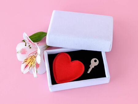 Red silk Valentine heart and a key on black velvet into a white jewelry gift box on a pastel pink background. Key to my heart, to open the heart and love concept. Top view.の写真素材