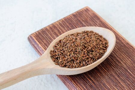 Whole flax seeds in a large wooden spoon on a brown cutting board over white rough background. Healthy food for lower cholesterol and preventing heart diseases. Top view.の写真素材