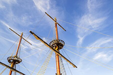 Scenic view of masts, sail yards with the lowered sails and rigging of a sailing ship against a clear blue sky with white clouds on a sunny day. Bottom view.の写真素材
