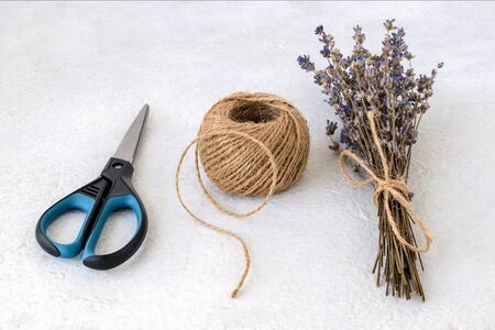 Natural hemp cord ball, scissors and dry lavender bouquet on a rough white surface. Roll of jute string or flax twine. Coarse rustic thread for souvenirs, macrame, craft or garden work. Top view.の写真素材