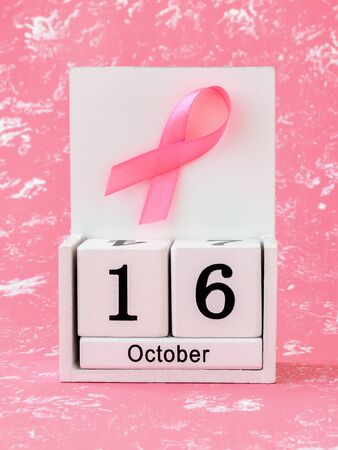 Pink ribbon of breast cancer awareness on a white wooden perpetual calendar with date 16 october. International breast cancer awareness month. Healthcare.の写真素材