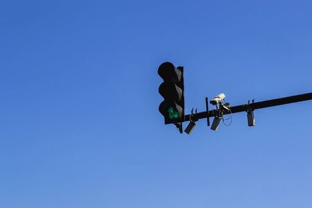 Traffic light with green color, outdoor surveillance camera and few sensors installed on a pole above a roadway. Modern automatic traffic control. Copy space. Against a blue sky.の写真素材