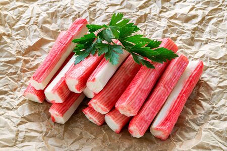 Heap of surimi crab sticks with parsley on a crumpled parchment paper. Seafood and ingredient for salads. Healthy eating and cook at home. Front view.の写真素材