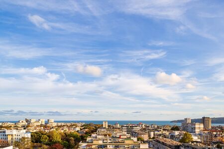 Beautiful blue sky with scenic fluffy clouds over seaside city on a sunny autumn day. Warm tranquil landscape with skyline. Soft focus.の写真素材