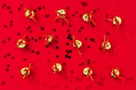 Christmas golden bells with bows on a red background with red stars. Festive flat lay for Christmas and New Year greeting card. Top view.の写真素材