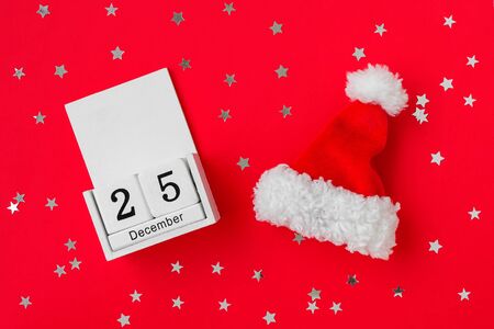 Santa Claus red hat and white wooden perpetual calendar with date 25 december on a red background...