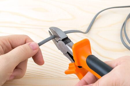 Woman hand holdins a metall side cutters with orange black rubber handles and cutting a wire over a rough wooden background. Electrician tool for repair and construction. Front view.の写真素材