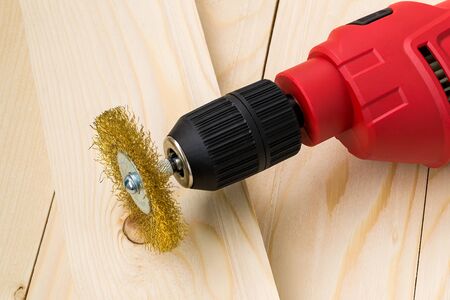 Red electric drill with round metal wire brush for cleaning of metal and wood and remove rust over rough wooden surface. Construction and repair. Front view.の写真素材