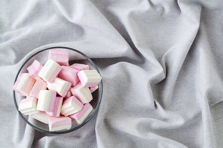 White pink fluffy marshmallows in a glass bowl on a gray picturesque flowing fabric. Sweet and tasty winter food. Delicious soft sweets. Copy space. Front view.の写真素材