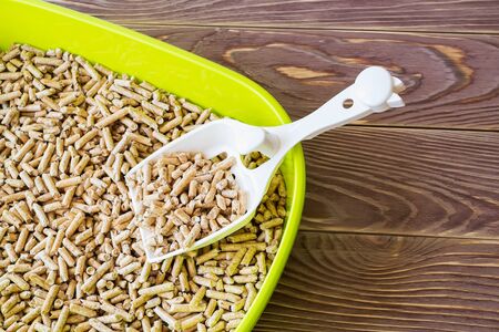 Close-up of green cat litter box with wooden pellets and scoop on a brown wooden floor. Plastic cat...