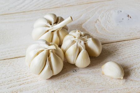 Three heads of raw garlic and one clove on a white wooden table. Spicy cooking ingredient. Vitamin healthy food. Vegetables and vegetarian. Top view.の写真素材