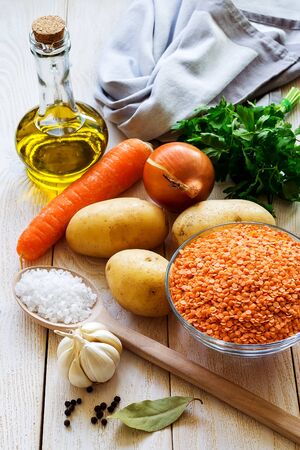 Ingredients for vegetable soup puree with red lentils: few yellow potatoes, carrot, onion and garlic, olive oil, parsley. On a white textured wooden table. Top view.の写真素材