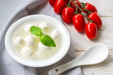Mini mozzarella cheese balls with brine, branch of red cherry tomatoes and porcelain spoon on a ...