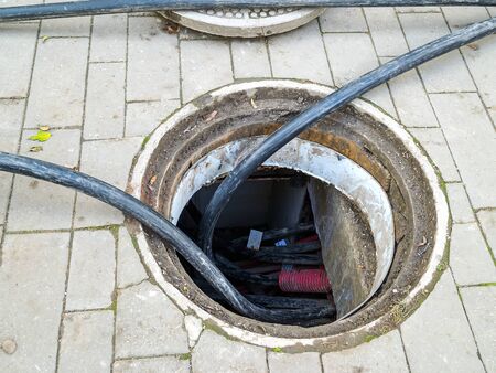 Opened manhole for cable replacement on the sidewalk. Laying of new cables in a hatch on a pavement....