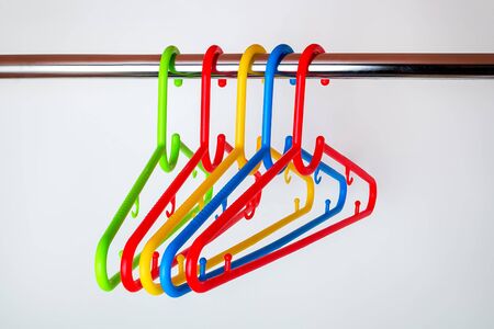 Five multicolored plastic clothes hangers on a rod in the closet. Set of new colorful plastic clothes hangers. Household items. Domestic life. Front view.の写真素材