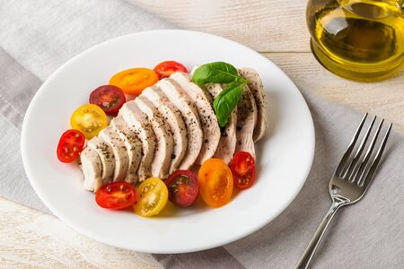Juicy chicken breast cooked under vacuum at low temperature. Sliced chicken fillet and halves of fresh cherry tomatoes on a white plate. Low calorie diet food. Front view.の写真素材
